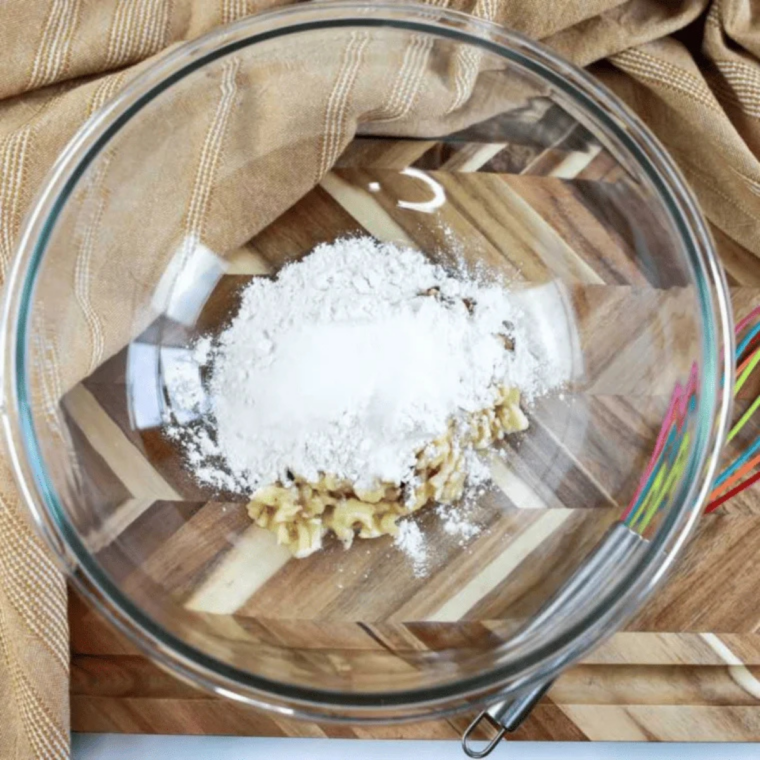 Flour, sugar, baking powder, vanilla, and salt added to mashed banana in a mixing bowl