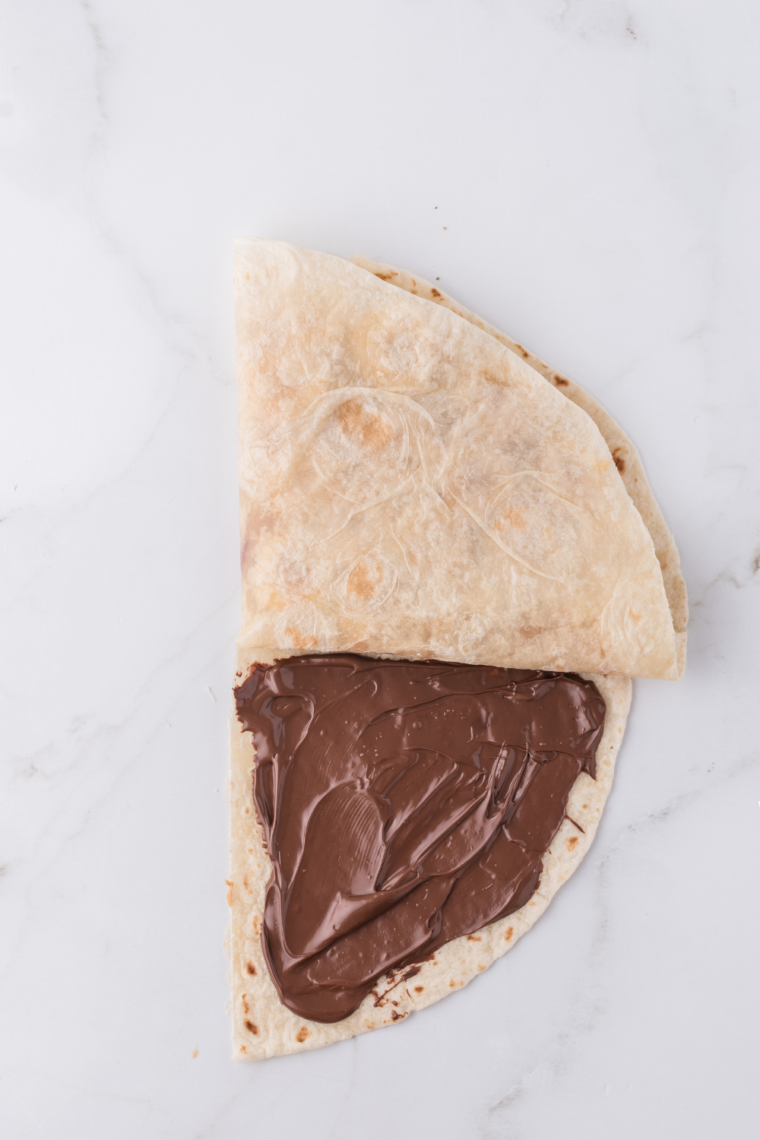 Sliced bananas arranged in a single layer over Nutella on a flour tortilla"