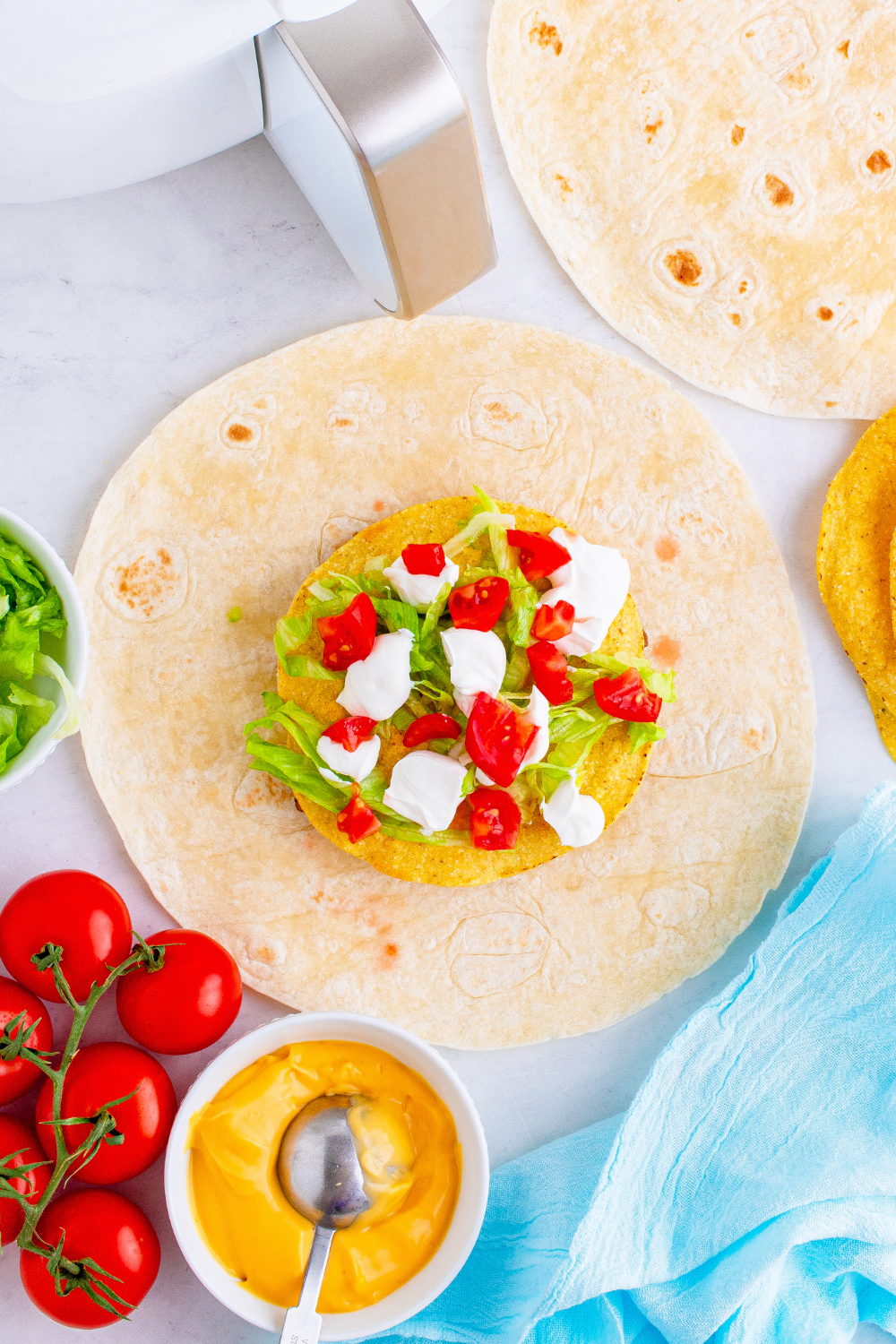 Crunchwrap being assembled with tostada shell, fresh toppings, and small tortilla, while large tortilla is folded tightly around the filling.
