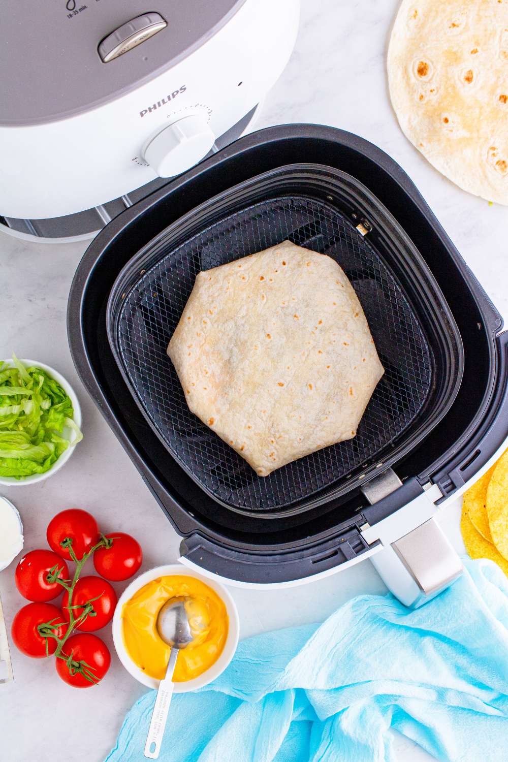 Crunchwrap placed seam side down in air fryer basket being sprayed with cooking oil before cooking.