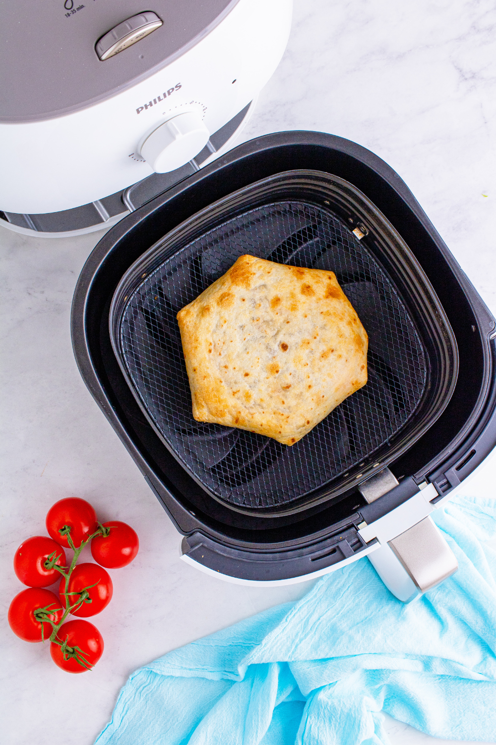 Crunchwrap being flipped in air fryer basket and sprayed with oil, cooking until golden brown and crispy on both sides.