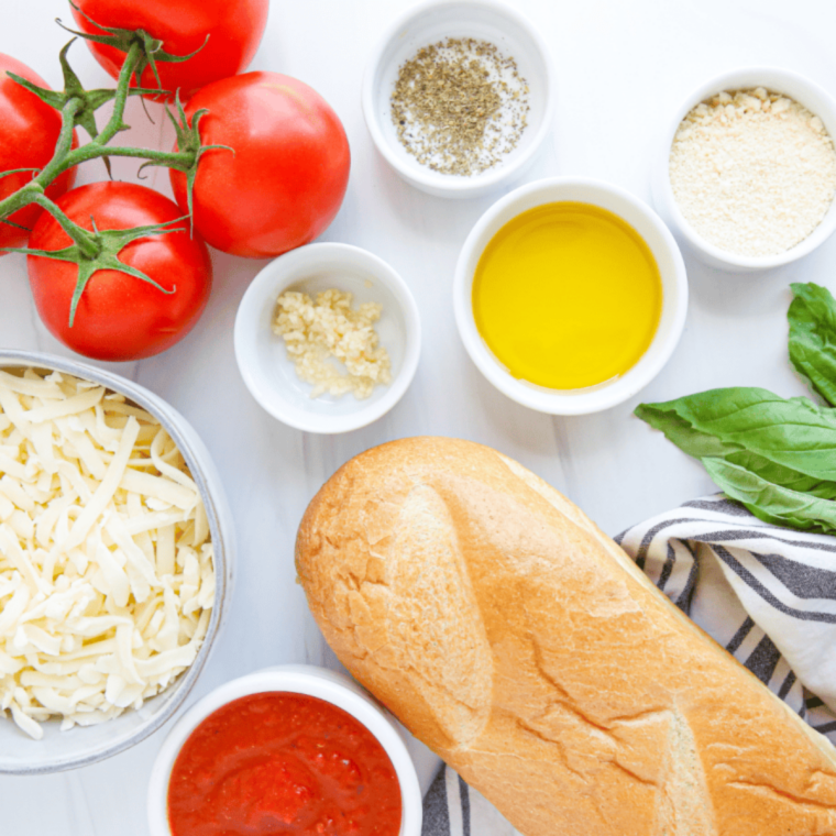Ingredients for homemade French bread pizza laid out: bread, mozzarella, sauce, tomatoes, basil