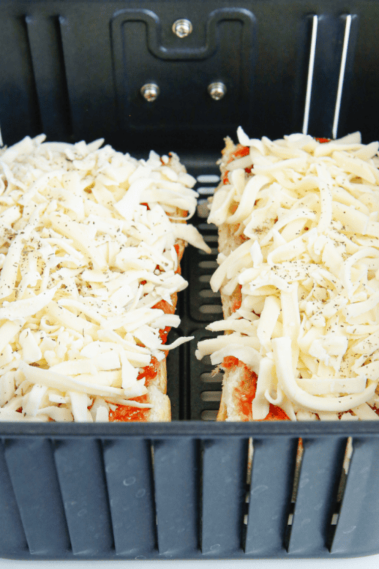Two French bread pizzas cooking in an air fryer basket at 375&deg;F with melting mozzarella cheese