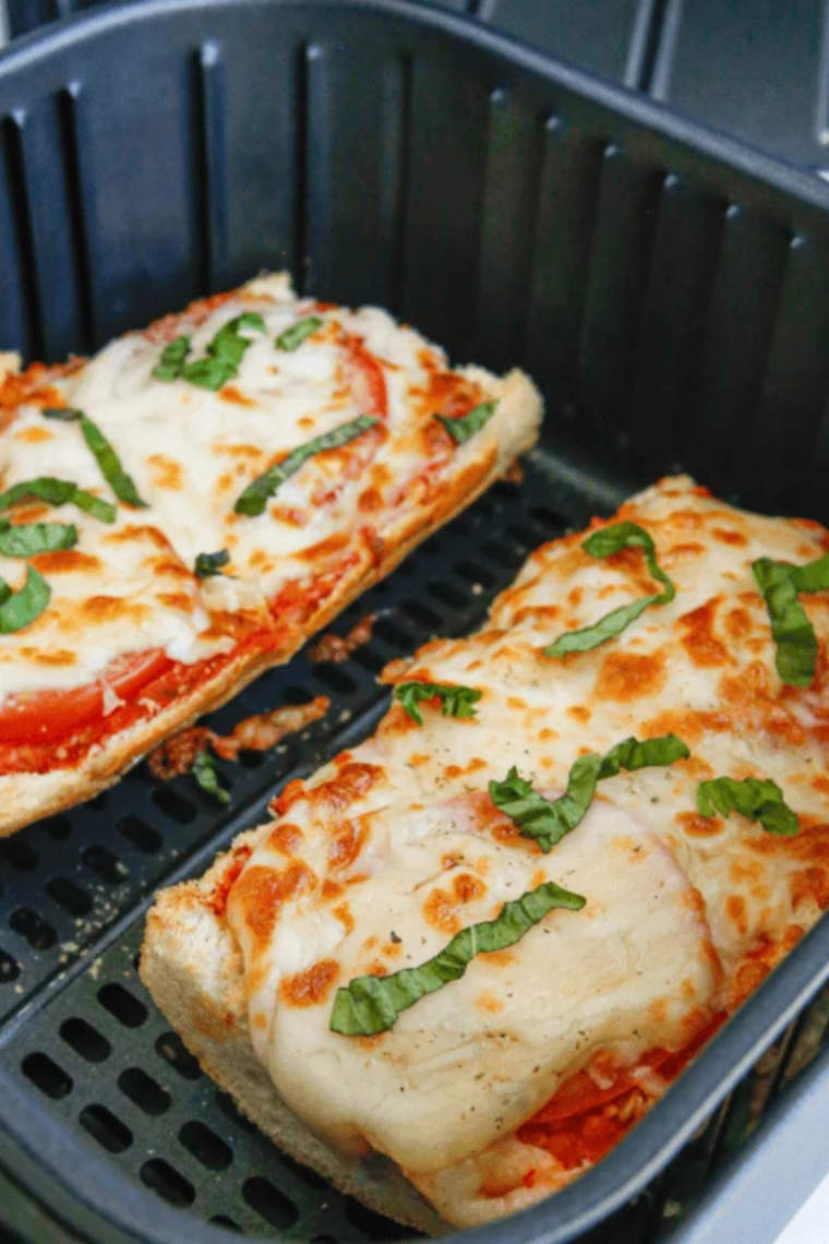 Air fryer French bread pizza garnished with fresh basil and sliced into serving pieces on a board
