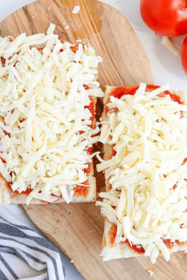 Layer the Toppings
Assembled French bread pizza topped with sauce, sliced tomatoes, mozzarella, Parmesan, garlic, and oregano