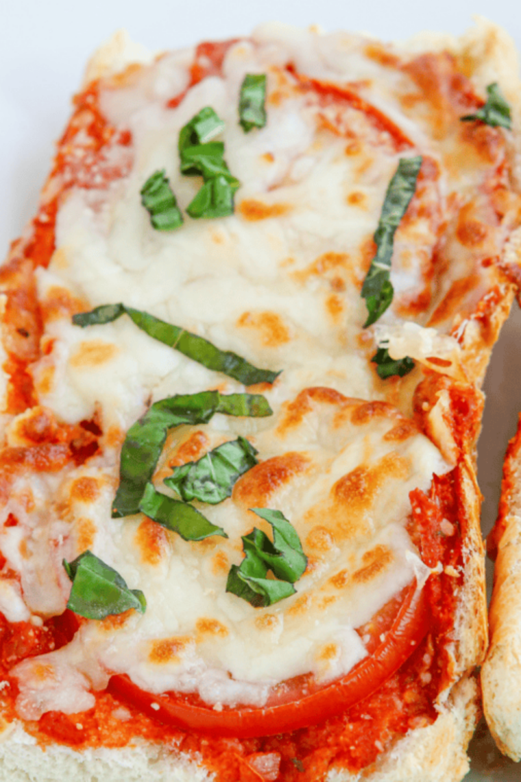 Finished air fryer French bread pizza sliced on a wooden board with melted mozzarella and fresh basil