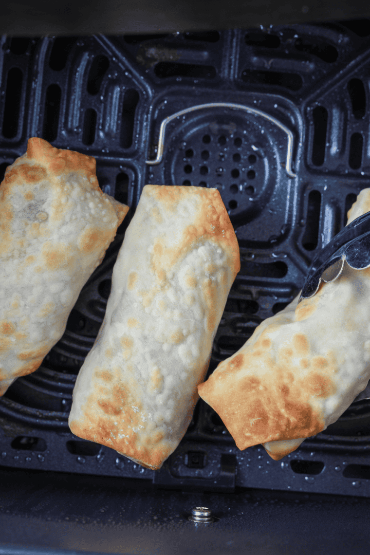 Egg rolls placed in a greased air fryer basket cooking until crispy and golden brown.