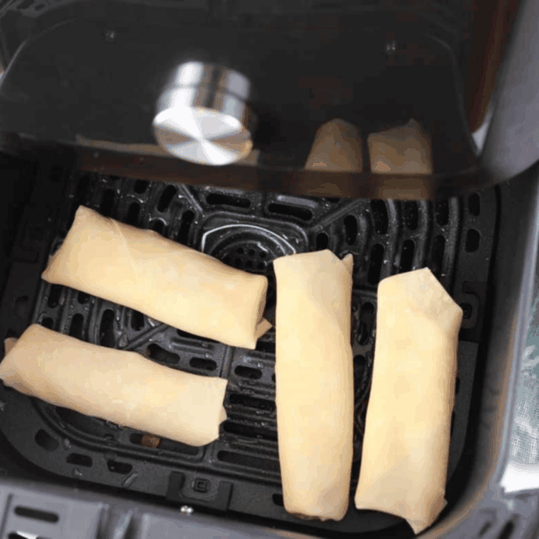 Egg rolls in air fryer basket, sprayed with cooking spray, ready to cook at 360°F until golden and crispy, served with dipping sauce.