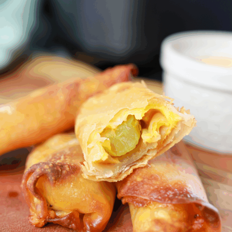 Golden crispy air fryer pickle egg rolls with melted cheese, ready to serve with dipping sauce.