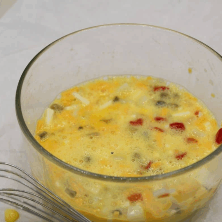 Mixing shredded cheese, diced vegetables, eggs, cream, salt, and black pepper in a small bowl for Air Fryer Veggie Egg Bites.