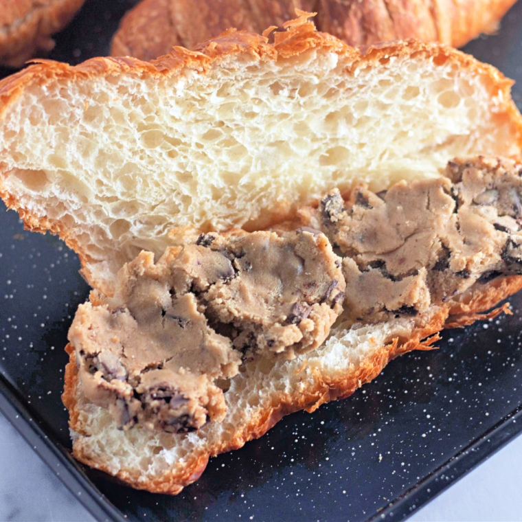 Knife slicing a large croissant lengthwise, about three-quarters of the way through, to make a pocket