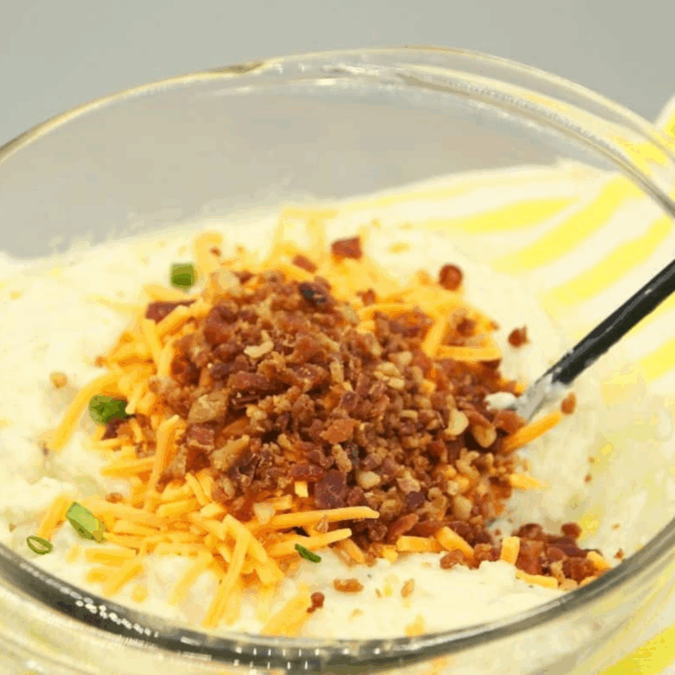Mixing mashed potatoes, egg, flour, cheddar cheese, bacon bits, and sliced green onions together in a medium bowl.
