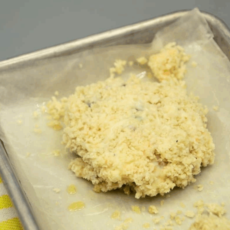Potato pancake formed, coated in panko breadcrumbs, placed on parchment-lined tray ready for freezing.