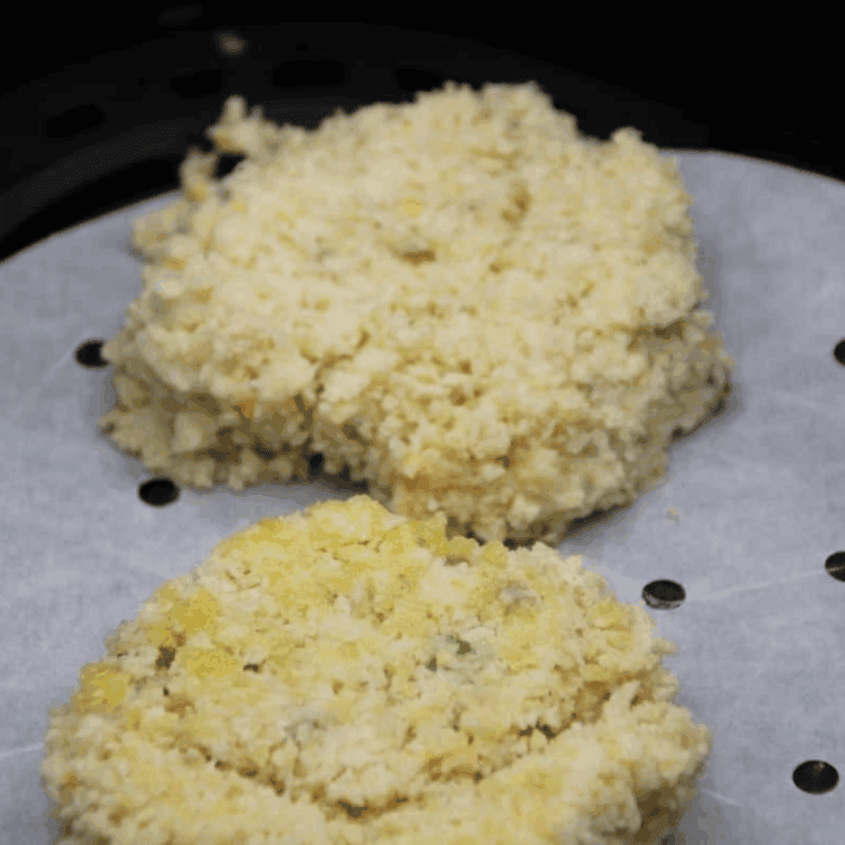 Frozen potato pancake placed on parchment paper in the air fryer, ready to cook at 380&deg;F, flipped halfway through.
