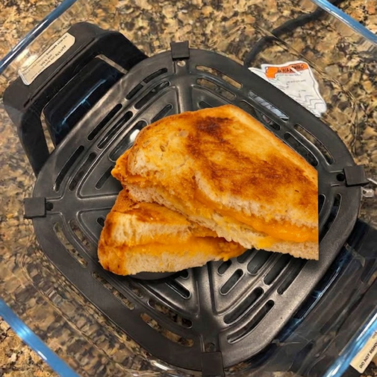 Grilled cheese sandwich being flipped with a spatula halfway through cooking in the Ninja Crispi