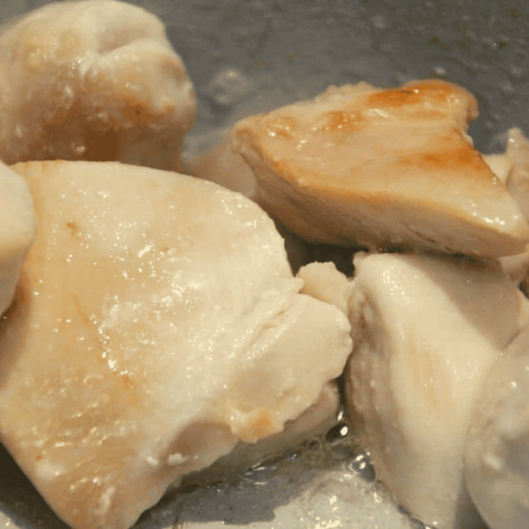 Seasoned chicken cubes browning in melted butter on the bottom of a Ninja Foodi pressure cooker, developing golden fond for chicken alfredo