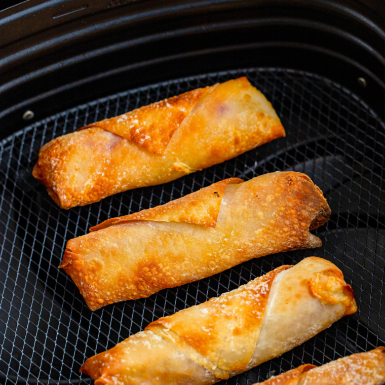 Golden brown ham and pickle egg rolls in the air fryer basket after cooking