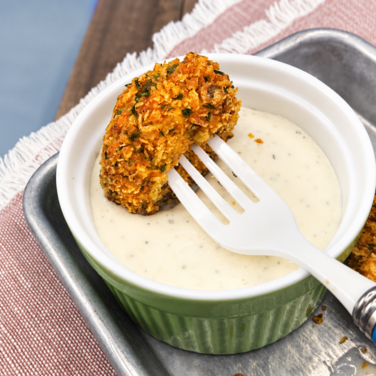 Bowl of golden Doritos-crusted pickle chips garnished with fresh herbs