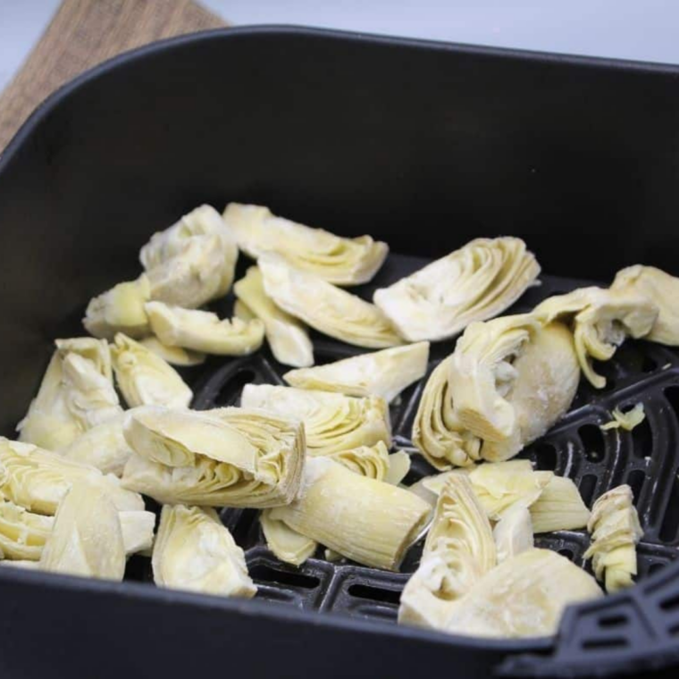 Frozen artichoke hearts tossed with oil and seasoning in an air fryer basket before cooking