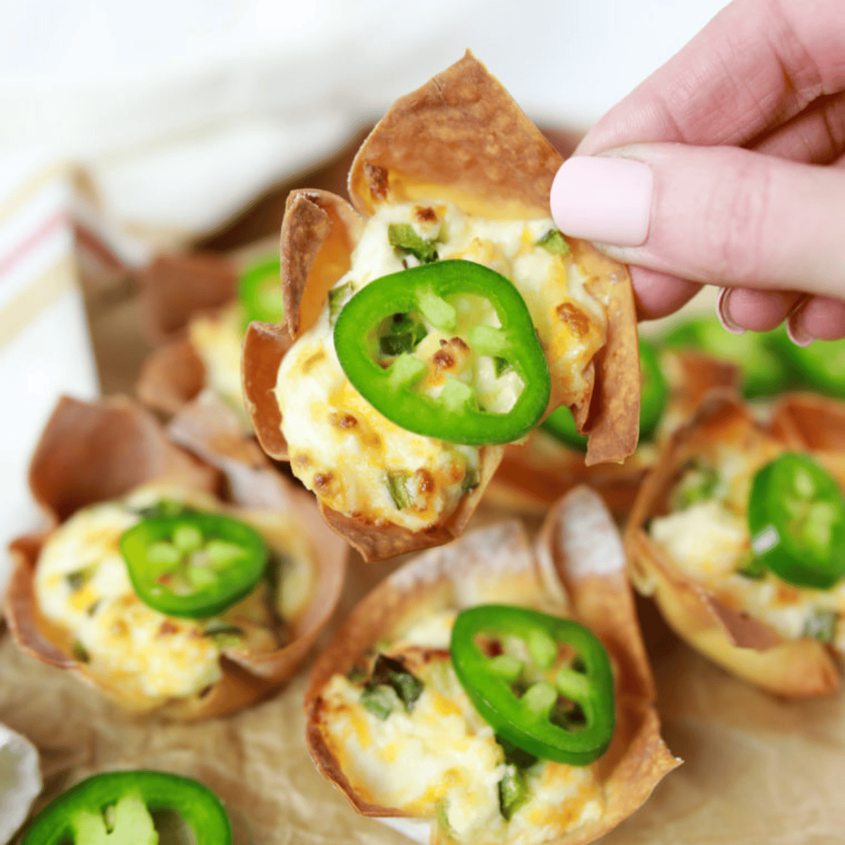 Close-up of a hand holding a jalapeno popper wonton cup topped with a jalapeno slice