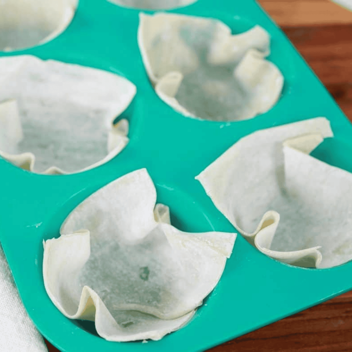 Wonton wrappers pressed into a muffin tin before air frying