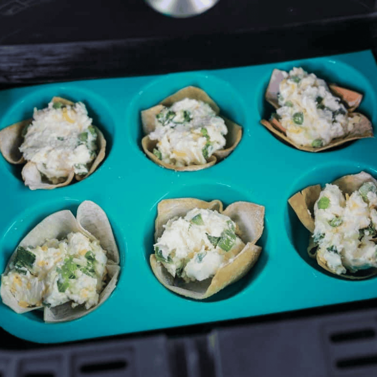 Filled jalapeno popper wonton cups in a muffin tin inside the air fryer basket
