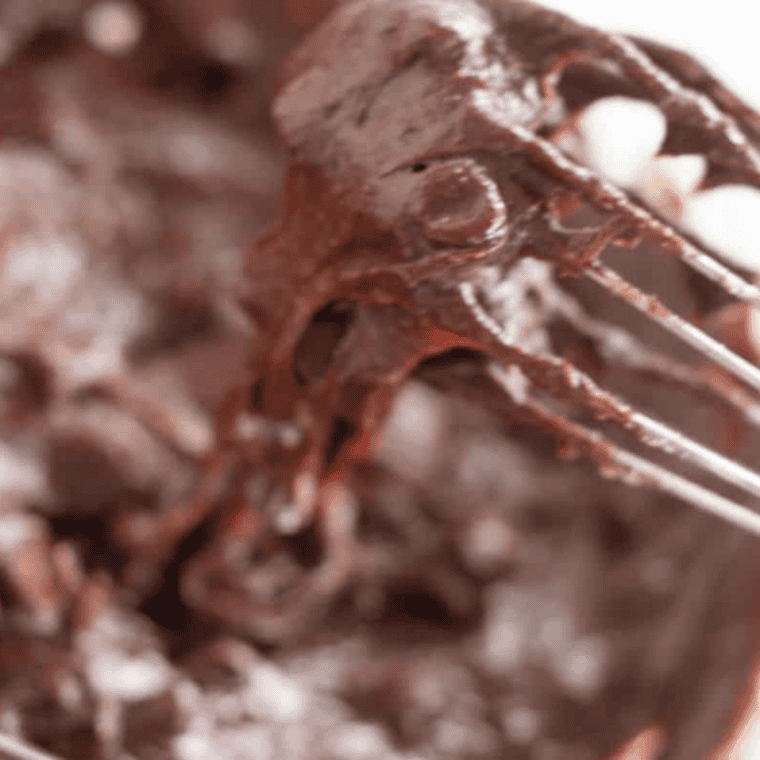 Brownie batter being mixed with sugar eggs and vanilla in bowl with melted chocolate base until smooth and glossy mixture