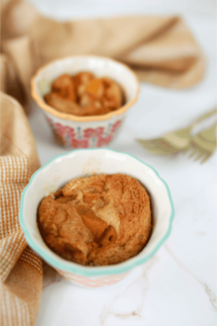 Mug filled with golden-brown peach cobbler cooked in an air fryer, topped with a scoop of vanilla ice cream.