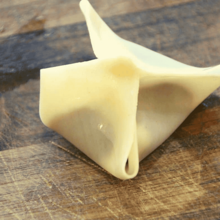 Folding wonton wrapper into a purse shape with raspberry filling inside.