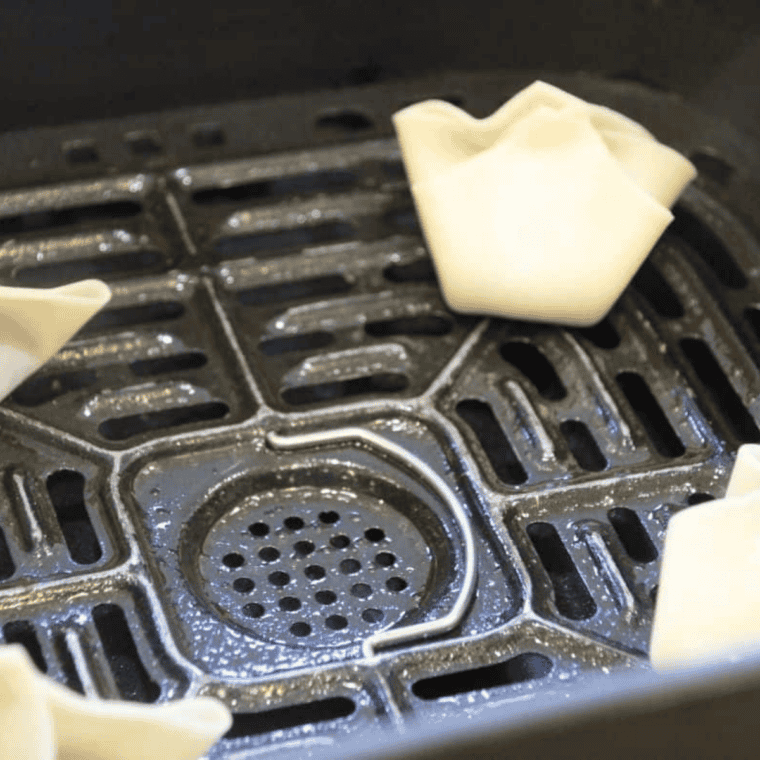 Raw raspberry wontons spaced out in an air fryer basket before cooking.