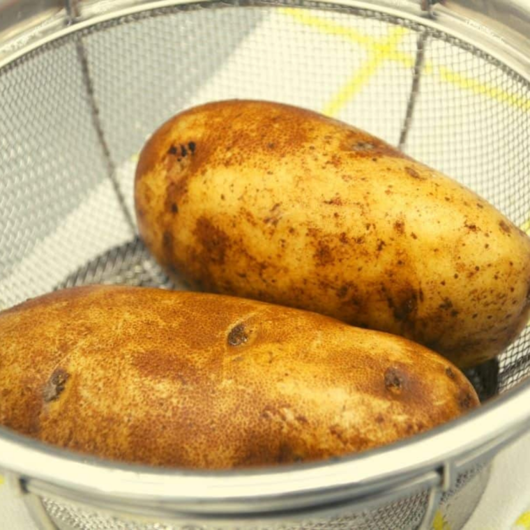 Russet potato being sliced into even quarter-inch fry sticks on a cutting board
