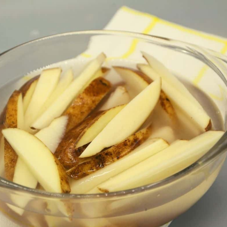 Cut potato fries submerged in a glass bowl of cold water