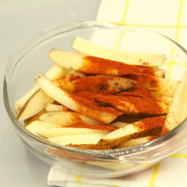 Potato fries tossed with olive oil and red chili seasoning in a large bowl