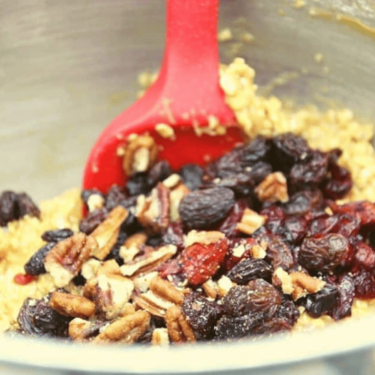 Folding dried cranberries, raisins, and nuts into cookie dough for even distribution.