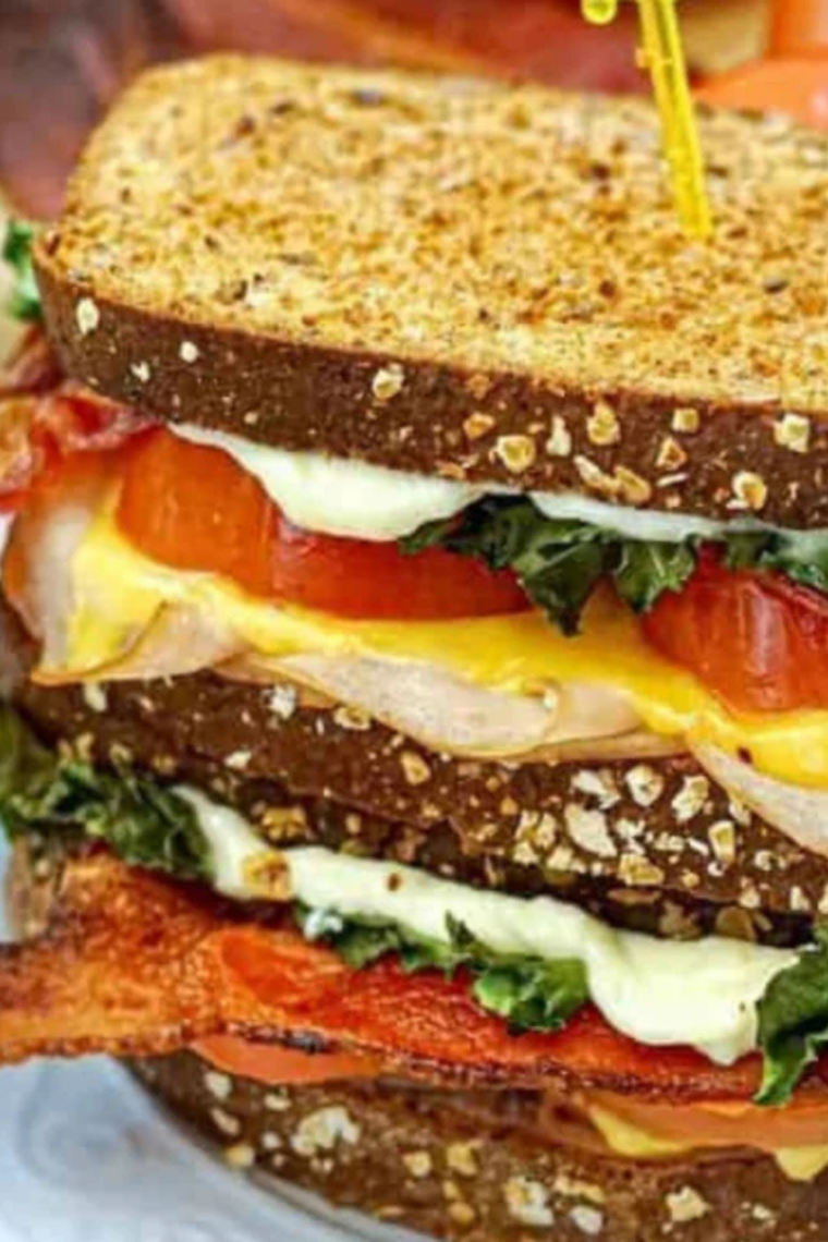 Close-up of a halved club melt sandwich showing layers of ham, turkey, bacon, melted cheese, and sauce