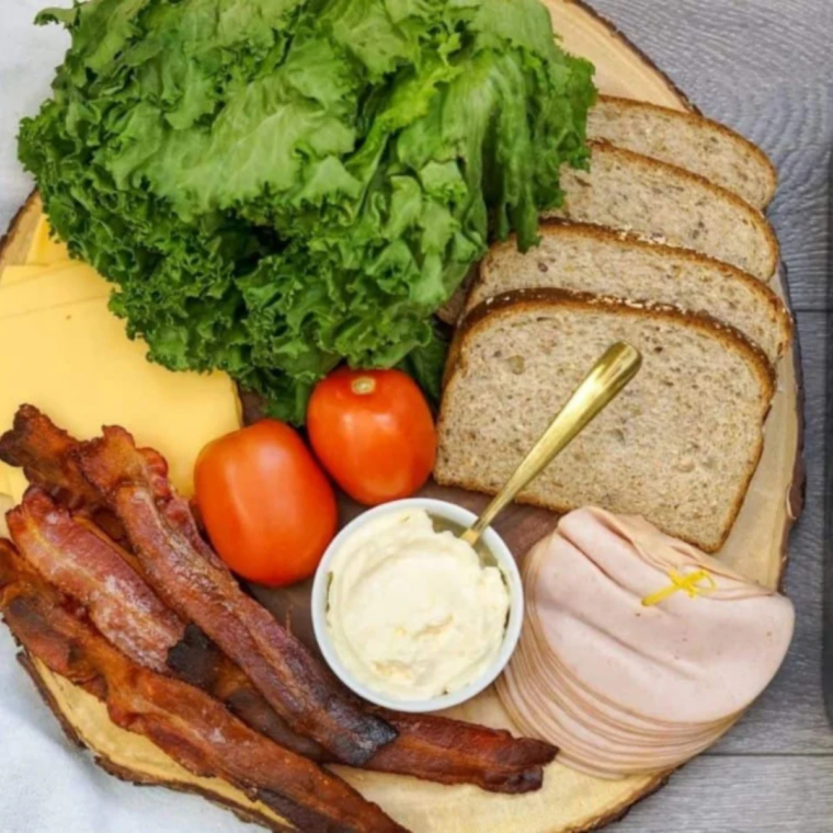 Ingredients for a Buc-ee's club sandwich, including brioche buns, deli ham, sliced turkey, thick-cut bacon, cheese, sun-dried tomato pesto, and spicy mayo