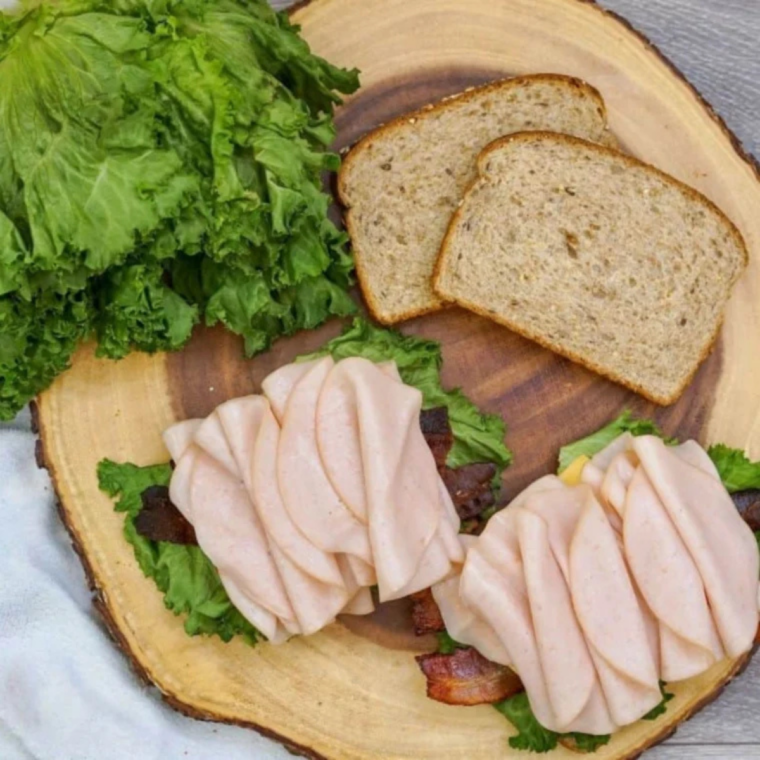 Layers of deli ham, turkey, and crispy bacon topped with a slice of cheese on a brioche bun