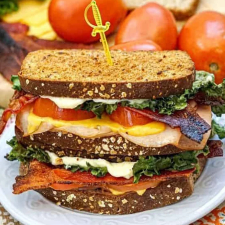 Copycat Buc-ee's club sandwich cut in half on a toasted brioche bun, stacked with ham, turkey, bacon, and melted cheese