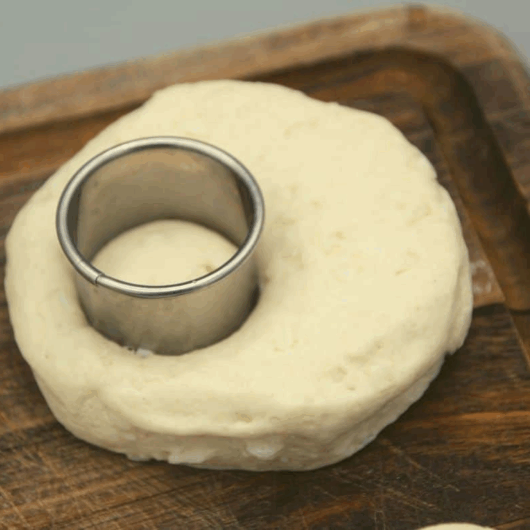 Punching out donut holes from biscuit dough using a cutter or bottle cap.