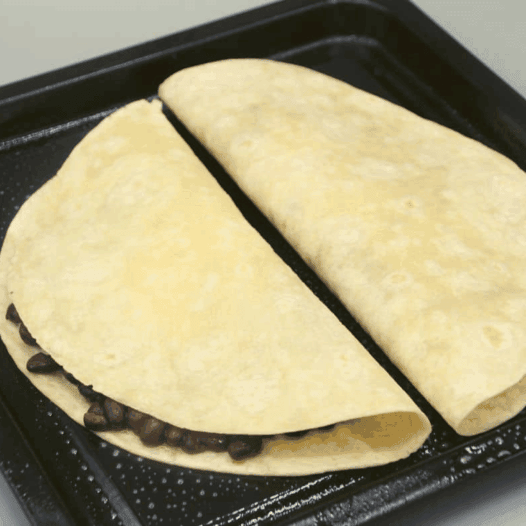 Black bean quesadilla cooking in air fryer basket until golden and crispy