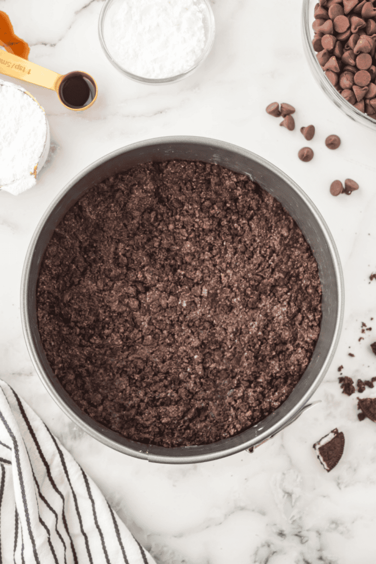 Pressing Oreo cookie mixture into a greased baking pan for cheesecake crust.