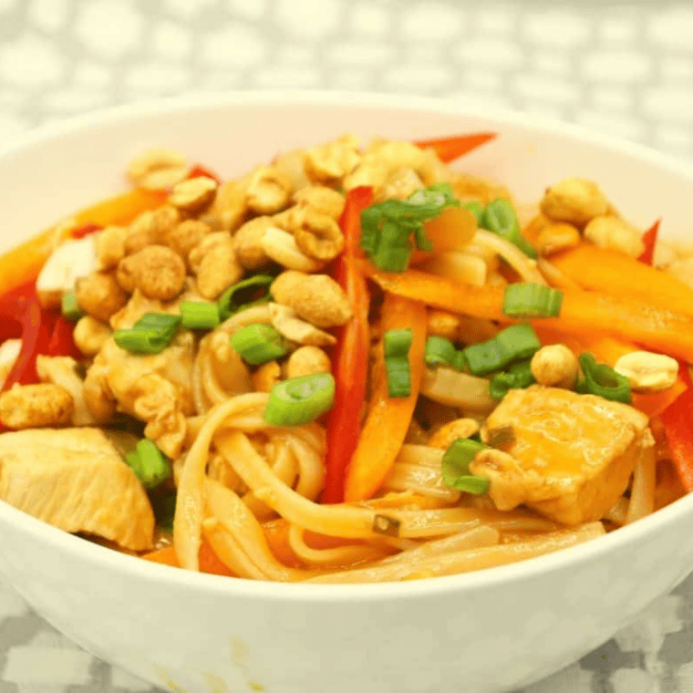Cooked pad thai noodles and chicken in the Ninja Foodi with sliced red and yellow bell peppers and peanuts being stirred in