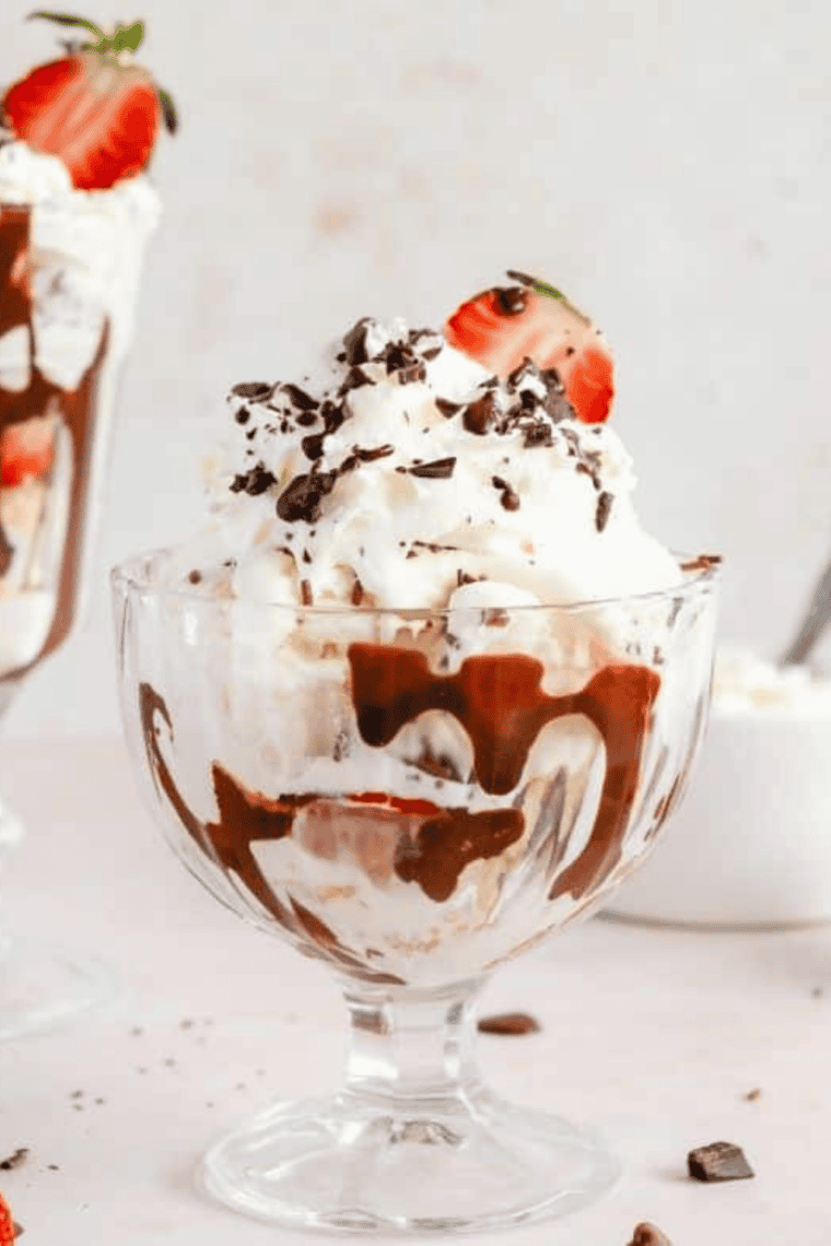 Air fryer blondie brownie cheesecake sundae layered with brownies, blondies, cheesecake slices, vanilla ice cream, whipped cream, strawberries, and hot fudge sauce in a dessert bowl.