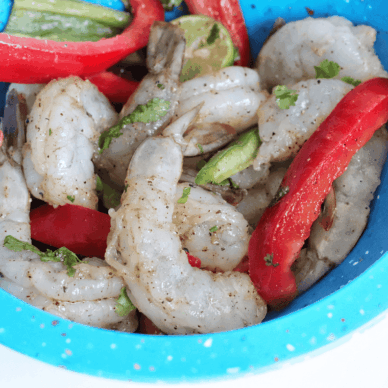 Red and green bell pepper strips mixed with thawed shrimp in a large bowl.