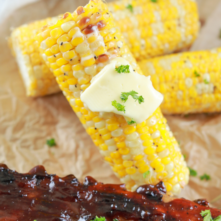 Close-up of corn on the cob being seasoned and grilled on a Blackstone flat top