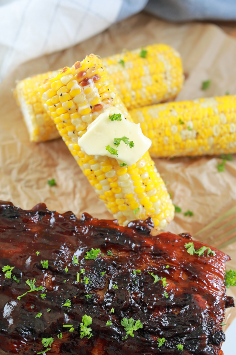 Fresh corn on the cob cooking directly on a hot Blackstone griddle, turning golden with grill marks.