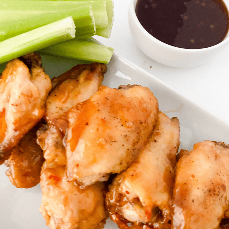 Plate of crispy chicken wings coated in sweet and tangy Hawaiian-style sauce, served hot and garnished for serving.