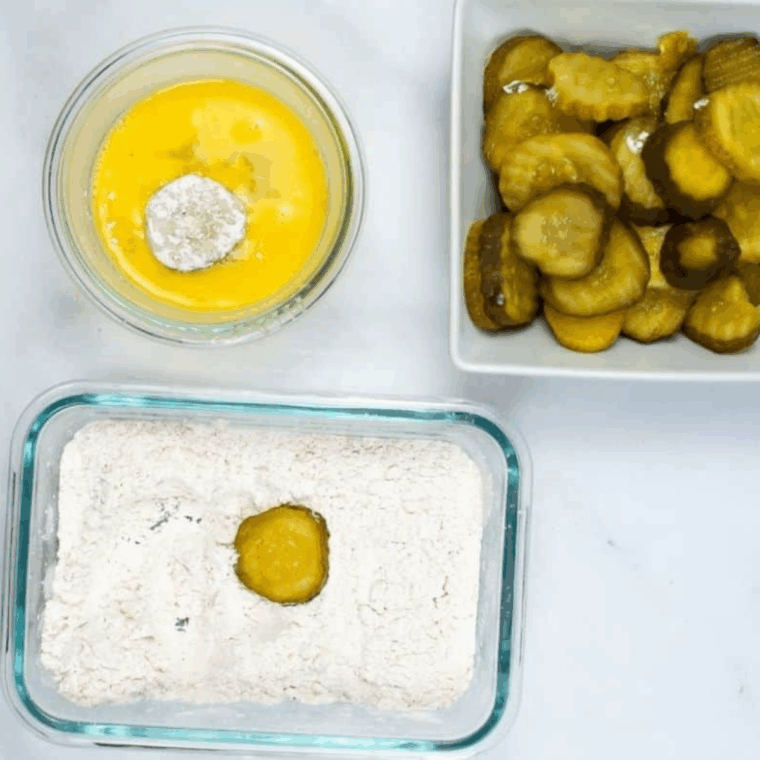Seasoned flour and cornstarch coating pickles beside beaten egg wash for breading process