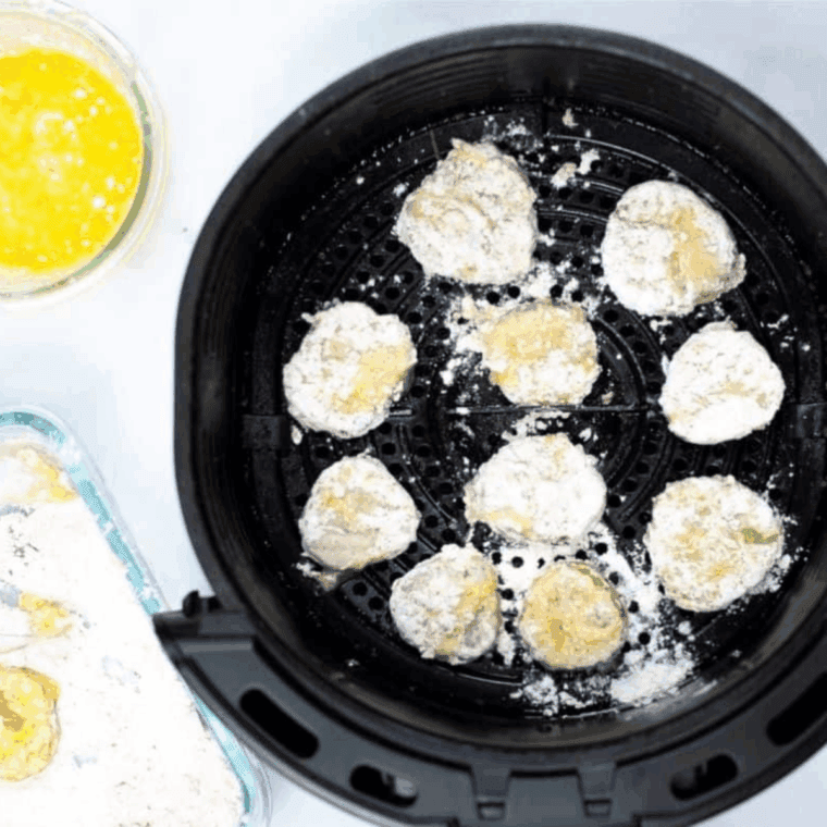 Breaded pickle slices arranged in air fryer basket, sprayed with oil before cooking