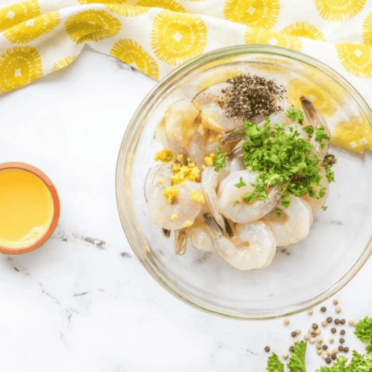 Raw shrimp sprinkled with salt, black pepper, and garlic powder in a bowl.